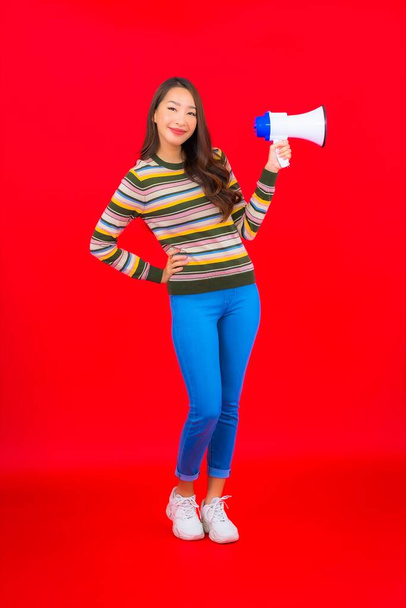 Portret pięknej młodej azjatyckiej kobiety z megafonem do komunikacji na czerwonym tle - Zdjęcie, obraz