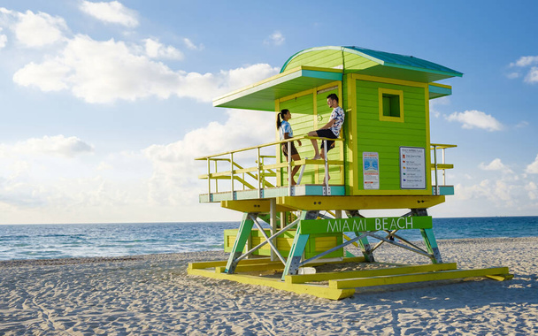 Маямі-Біч, подружжя на пляжі в Маямі-Флориді, жінки-рятувальники з Маямі-Азіатської Азії та чоловіки-ізгої на пляжі під час заходу сонця. Чоловік і жінка спостерігають за сходом сонця. - Фото, зображення