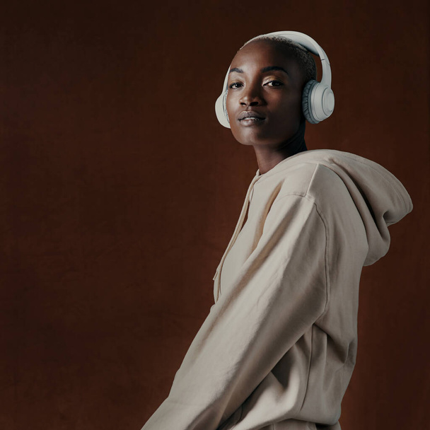 I rock to my own beat. Studio portrait of an attractive young woman wearing headphones and posing against a brown background - Foto, Bild