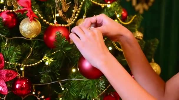 Hermosas manos femeninas cuelgan una bola de Navidad en un árbol de Navidad en el contexto de las decoraciones de Año Nuevo de cerca. Feliz Navidad.. - Metraje, vídeo