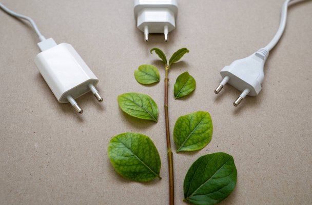 Закройте фотографию нескольких разъемов для зарядки и зеленых листьев. Концепция энергосбережения и снижения потребления электроэнергии. - Фото, изображение