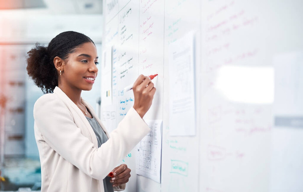 Project manager writing on a whiteboard to plan ideas and visualize business strategy. Focused, confident and thoughtful businesswoman showing ambition and dedication while working in an office. - Foto, imagen