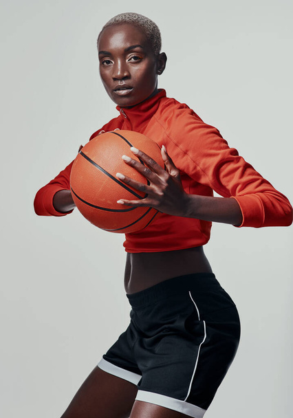And now for the power play. Studio shot of an attractive young woman playing basketball against a grey background - Foto, imagen