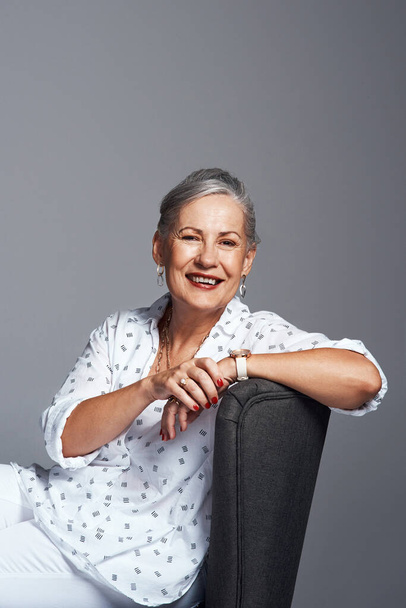 Being happy never gets old. Studio shot of a senior woman sitting on a chair against a grey background - Valokuva, kuva