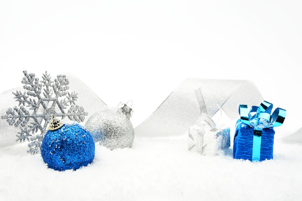 Silver and blue christmas glittering baubles with ribbon on snow - Fotó, kép