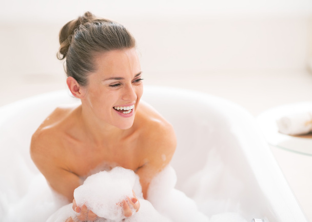 Happy young woman playing with foam in bathtub - 写真・画像