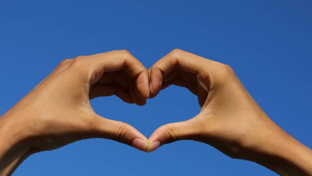 две соединенные руки, образующие сердце на голубом небе на заднем плане - Фото, изображение