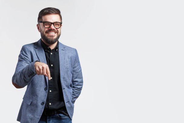 Κοντινό πλάνο του νεαρού επιχειρηματία που φοράει γυαλιά και έξυπνο casual κοστούμι, χαμογελώντας στην κάμερα, απομονωμένο σε γκρι φόντο - Φωτογραφία, εικόνα