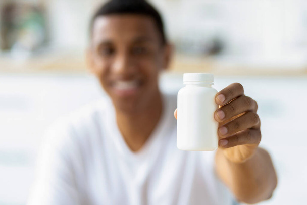 Happy young african american man holding capsules and open bottle. Painkiller, headache medication or vitamins concept - Photo, image