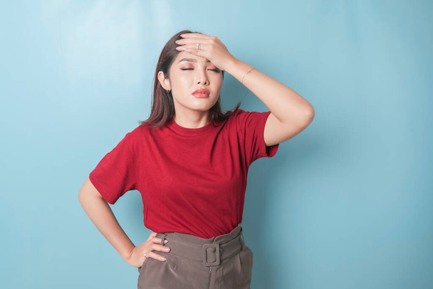 A portrait of an Asian woman wearing a red t-shirt isolated by blue background looks depressed - Foto, afbeelding