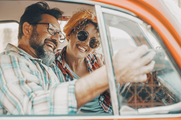 Ευτυχισμένο ζευγάρι που διασκεδάζει μέσα σε ένα αυτοκίνητο κατά τη διάρκεια ταξιδιωτικής περιπέτειας. Χαρούμενος άντρας και γυναίκα χαμογελούν και γελούν πολύ μαζί. Οι άνθρωποι απολαμβάνουν το ταξίδι με το αυτοκίνητο στη φιλία και τη σχέση. Έννοια της κίνησης - Φωτογραφία, εικόνα