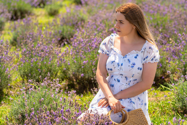 Pensive young woman kneeling in a field of lavender looking to the side with a contemplative expression - Fotoğraf, Görsel