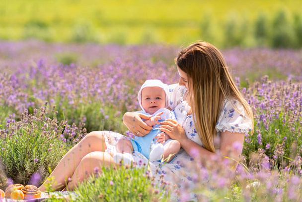 Happy little baby gurgling and smiling at camera as it lies in its mothers arms outdoors in a field of purple lavender - Foto, afbeelding