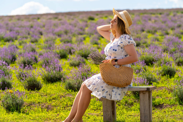 Young woman enjoying the sumner sunshine in lavender fields seated on a rustic wooden bench - Foto, Bild