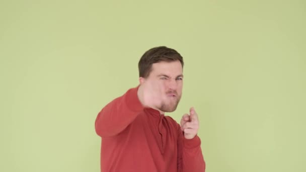 Handsome young man in a red sweater funny shows shots from a gun with his hands isolated on the background in the studio, a man shows his great mood on camera - Footage, Video