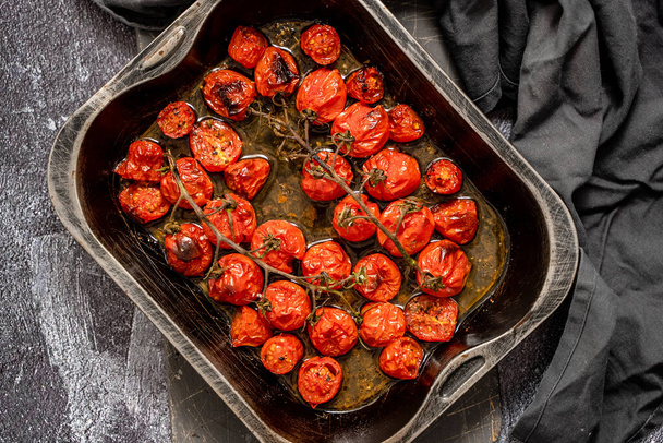 Поднос из жареных красных помидоров черри с чесноком, травами и оливками. Вид сверху, плоский - Фото, изображение