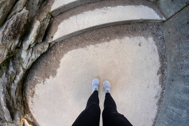Вид сверху вниз на женщину в черных ногах и удобной обуви, сидящую на бетонных ступеньках - Фото, изображение