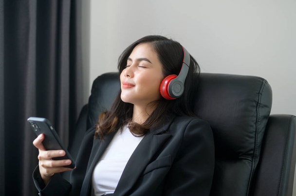 A Young relaxing business woman using smartphone and listening to music in modern office. - Fotó, kép