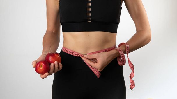 Una donna con una figura snella misura la sua vita con un metro, frutta nelle sue mani. Foto di alta qualità - Foto, immagini