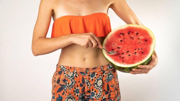 A woman in beachwear eats watermelon with a spoon - summer atmosphere. High quality photo - Photo, Image