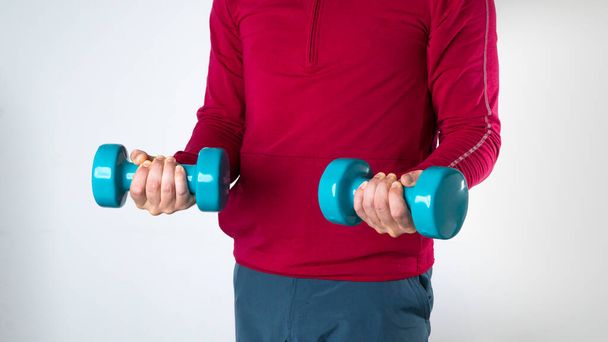 A man in a sports fom holds dumbbells on a white background. High quality photo - Photo, Image