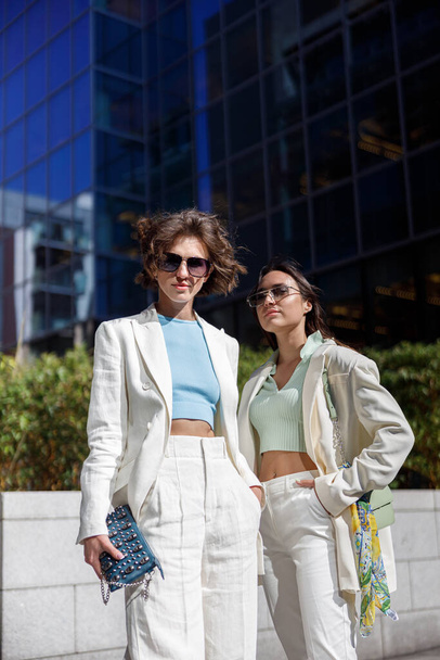 Two fashionable woman friends standing on background of modern buildings. High quality photo - Foto, imagen