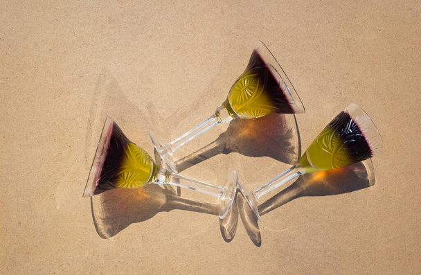 3 crystal glasses with two-color fruit jelly lie on a beige background, top view. Bright sun, interesting shadows. Holiday and fun atmosphere. Delicious summer refreshing desserts - Foto, afbeelding
