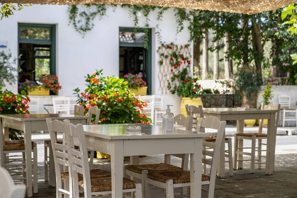 Greek outdoors tavern restaurant with empty white table and chair at Kithira Ionian islands Milopotamos village destination Greece. Pots with flowers everywhere. - 写真・画像