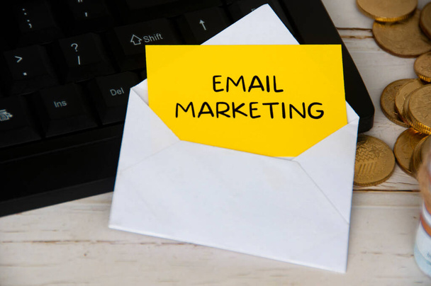 Email κείμενο μάρκετινγκ σε κίτρινο σημειωματάριο σε ένα φάκελο στον υπολογιστή πληκτρολόγιο με χρυσά νομίσματα. Online επιχειρηματική ιδέα - Φωτογραφία, εικόνα