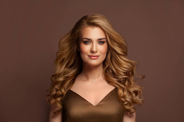 Attraktive junge blonde Frau mit langen welligen Haaren und freundlichem Lächeln auf braunem Hintergrund - Foto, Bild