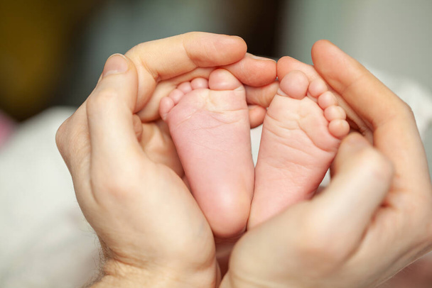 Τα χέρια του μπαμπά αγγίζουν τα πόδια της αξιολάτρευτης νεογέννητης κόρης του. - Φωτογραφία, εικόνα