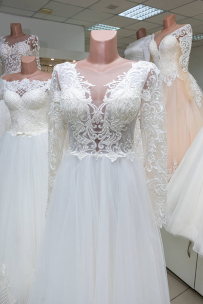 A beautiful white wedding dress on a mannequin. A close-up of a dress against other wedding dresses in a bridal shop. - Foto, afbeelding