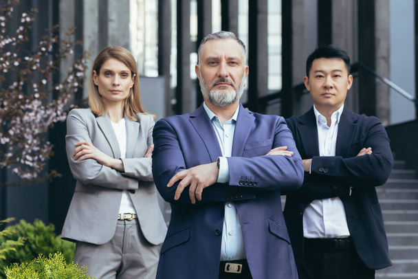 Portrait of serious diverse business team, employees with boss together looking at camera seriously and thoughtfully, group of business people outside office in business suits - Фото, зображення