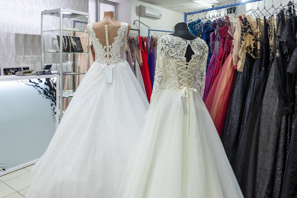 Дві білі весільні сукні на тлі темних вечірніх суконь у магазині весільних суконь
. - Фото, зображення