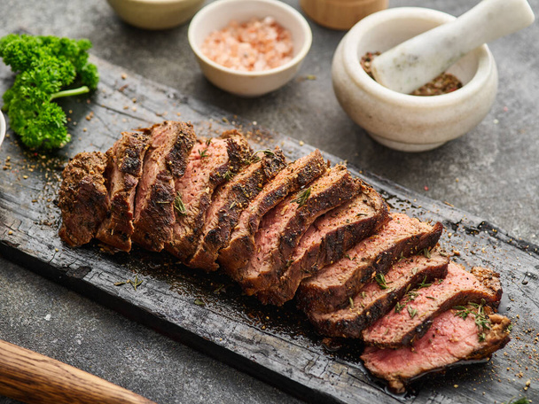 Grilled sliced beef steak on cutting board over grey table. Beef tenderloin steak recipe. - Photo, Image