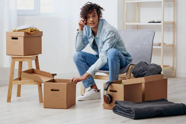 portrait of a man sitting on a chair unpacking with box in hand moving sorting things out. High quality photo - Photo, Image