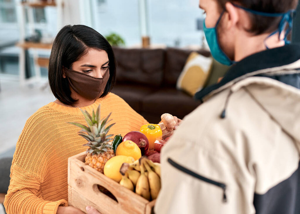 The home delivery business is booming during lockdown. a masked young woman receiving a delivery of fresh fruit and vegetables at home - Foto, Bild