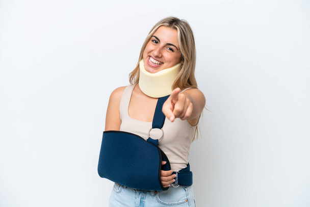 Woman with broken arm and wearing a sling isolated on white background pointing front with happy expression - 写真・画像
