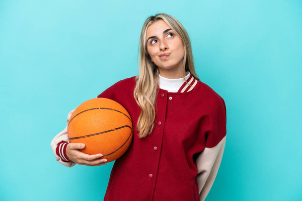 Young caucasian basketball player woman isolated on blue background and looking up - Фото, зображення