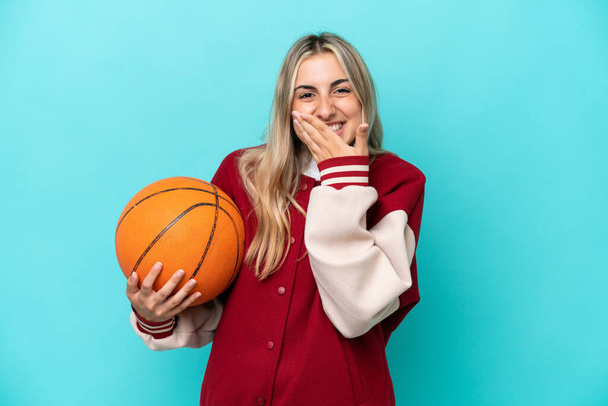 Young caucasian basketball player woman isolated on blue background happy and smiling covering mouth with hand - Foto, Bild