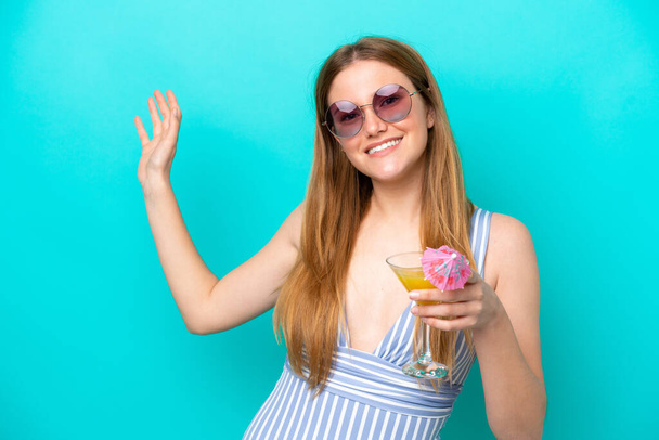 Young woman isolated on blue background in swimsuit and holding a cocktail - Fotoğraf, Görsel