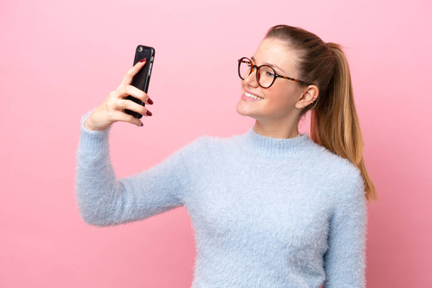 jonge Kaukasische vrouw geïsoleerd op roze achtergrond het maken van een selfie - Foto, afbeelding