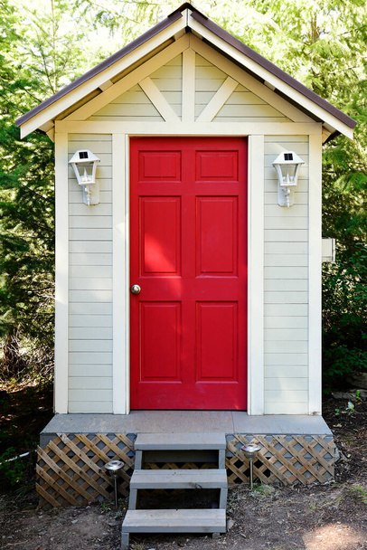 Изображение открытого компостирующего туалета с ярко-красной дверью и солнечными лампами.  - Фото, изображение