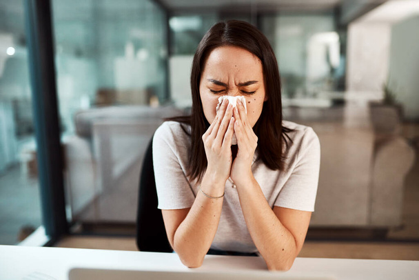 Dealing with a stuffy and runny nose. a young businesswoman blowing her nose while working in an office - Valokuva, kuva