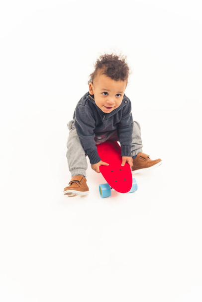 cute excited african american toddler boy sitting on the skateboard - white background. High quality photo - Fotó, kép