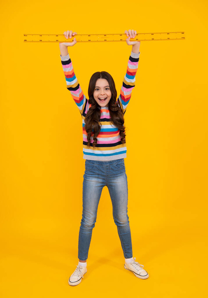 Amazed teenager. Measuring school equipment. Schoolgirl holding measure for geometry lesson, isolated on yellow background. Student study math. Excited teen girl - Foto, imagen