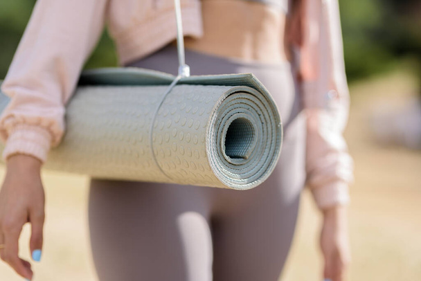 Horizontal closeup of fit woman in purple clothing carrying rolled up yoga mat - Foto, Imagem