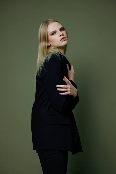 Art Fashion Fotoshooting. Professionelles blondes Model umarmt sich mit beiden Händen und blickt mit halb gedrehten Blicken in die Kamera, die auf grünem Hintergrund im Studio posiert. Hochwertiges Foto - Foto, Bild