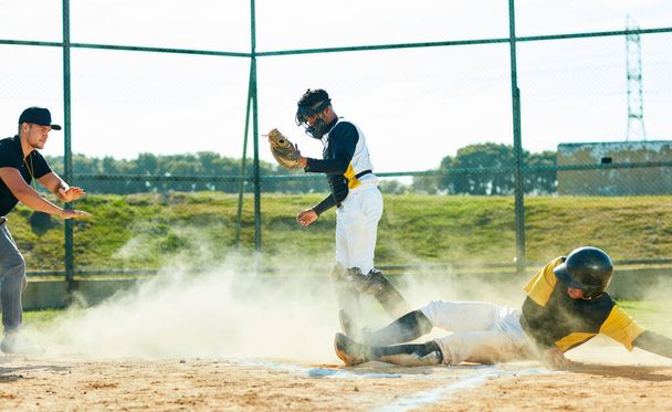 Η σκόνη είναι η παιδική χαρά του. Πλήρες πλάνο ενός νεαρού παίκτη του μπέιζμπολ που φτάνει στη βάση κατά τη διάρκεια ενός παιχνιδιού στο γήπεδο - Φωτογραφία, εικόνα