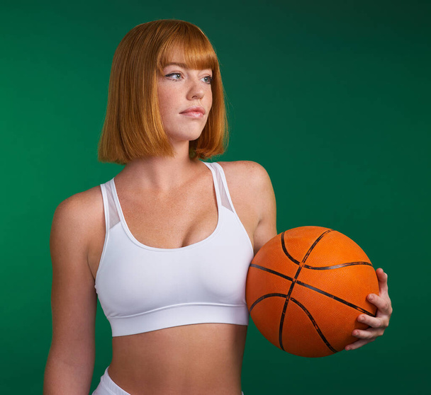 Μάθε το σώμα σου. μια ελκυστική νεαρή αθλήτρια που στέκεται μόνη της και κρατά ένα μπάσκετ σε ένα πράσινο φόντο στο στούντιο - Φωτογραφία, εικόνα
